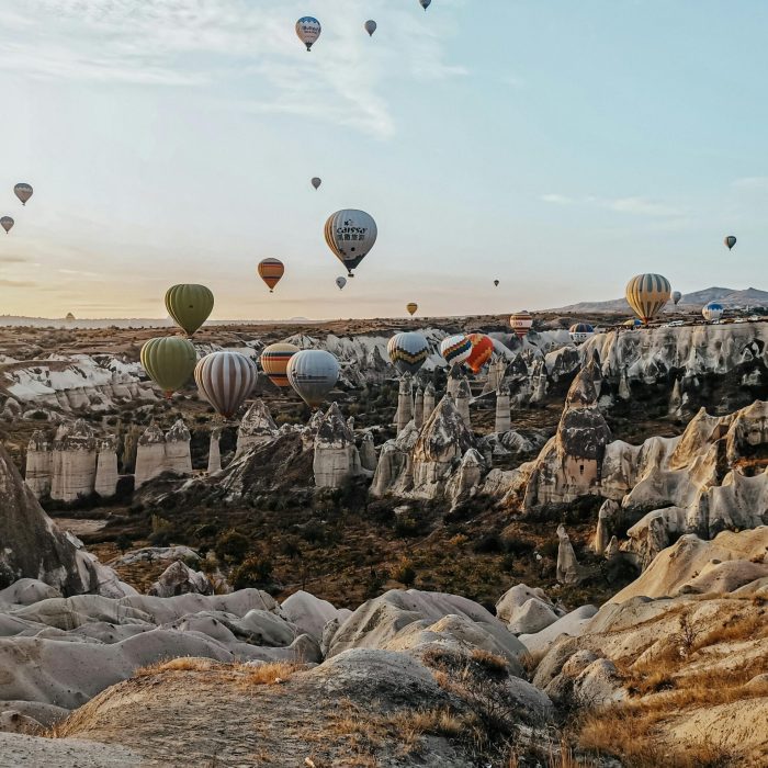 Breathtaking view of hot air balloons soaring over Cappadocia's unique rock formations during sunrise.